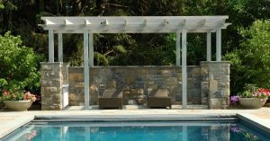 white pergola shade structure next to pool area attached to stone base